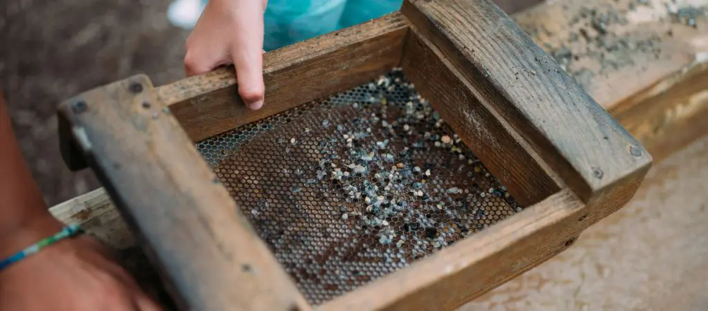 Child's hand holding a sifting container while mining for gems outside.