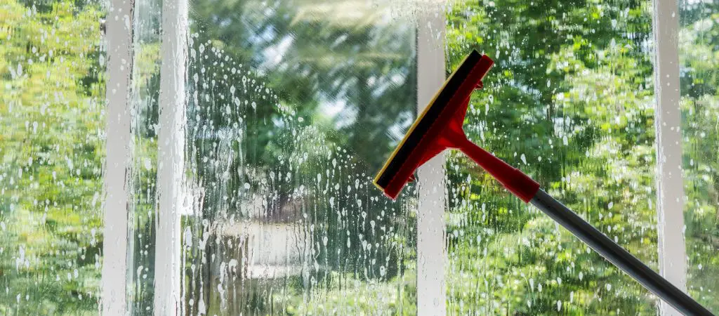 Large squeegee wiping away the water from a large window looking out to wooded views