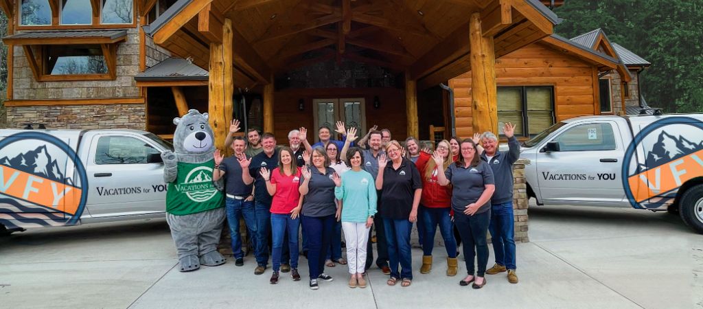 Georgia Cabins for YOU team and mascot Barry the Bear wave at the camera in front of a mountain lodge.